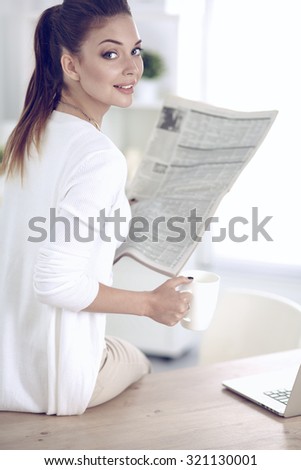 Cute businesswoman holding newspaper sitting at her desk in office