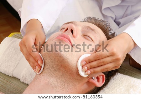 Female hands cleaning man\'s face with cotton swabs in a spa center