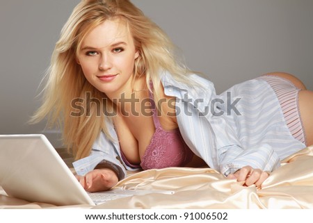 A sexy woman lying on the bed with laptop, isolated on grey background