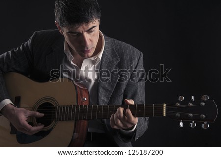 Man playing guitar against black background.