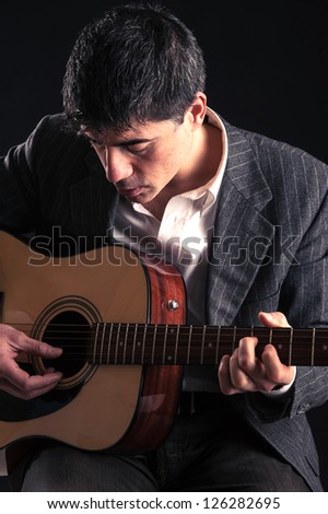Man playing guitar against black background.