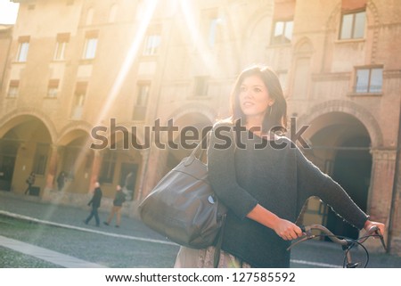 Woman walking with bicycle in Saint Stephen square, Bologna, Italy. Back light.