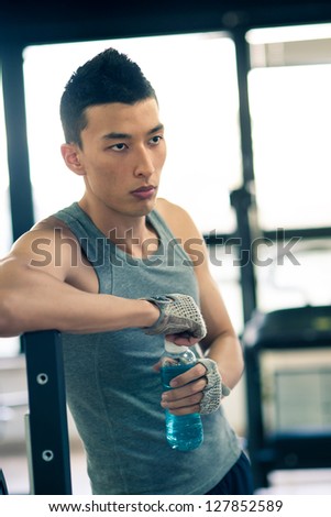 Young asian man having a rest drinking a beverage in the gym.
