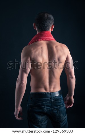 Back view of young man shirtless with red towel against black background.