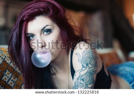 Sensual portrait of beautiful tattooed red head girl with chewing gum.