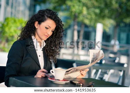 Business woman reading newspaper outdoors sit in a bar. Shallow depth of field.