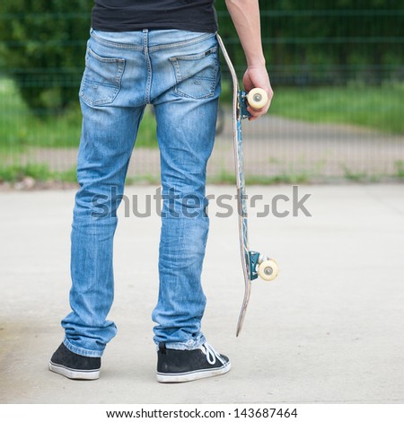 Man from behind holding skateboard.