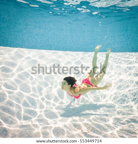 Woman swimming underwater with pink bikini in swimming pool.