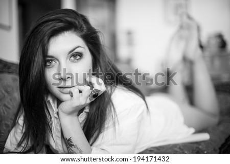 Sensual portrait of beautiful girl with tattoo lying on sofa. Black and white image.