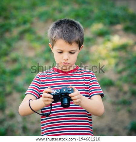 Portrait of child with digital compact camera outdoors.
