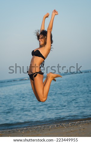 Jumping woman wearing bikini at the beach.