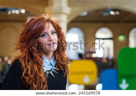 Portrait of young smiling redhead woman inside public library.