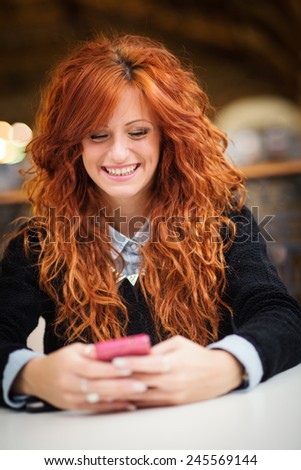 Smiling redhead woman using mobile phone in public library.