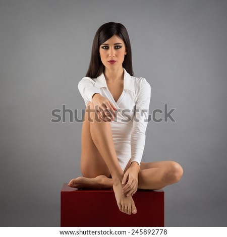 Woman full body portrait sit on red cube against grey background.