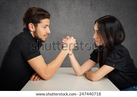 Young couple studio portrait doing arm wrestling against grunge background.
