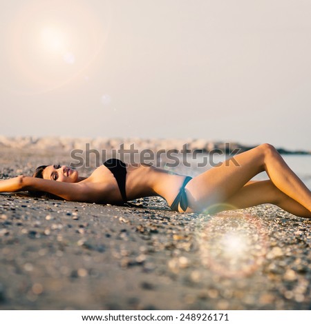 Sexy woman wearing bikini laying on the beach. Filtered image with flare.