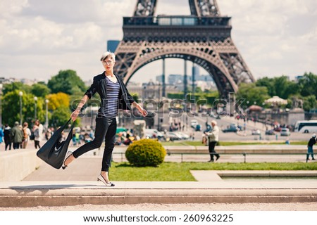 Fashion young blonde woman walking portrait in front of the Eiffel Tower in Paris, France. Filtered image.