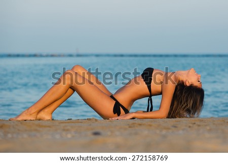 Sensual woman wearing black bikini laying on the beach at sunset.