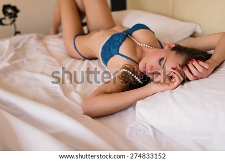 Sensual young blonde woman portrait wearing lingerie laying on the bed in hotel room. Filtered image.