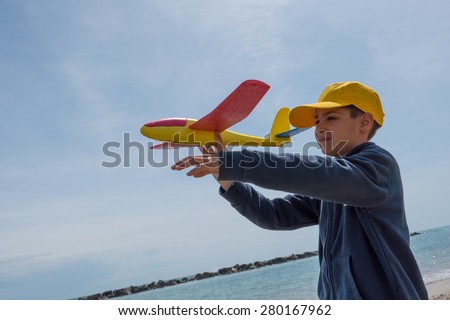 Happy kid playing with toy airplane against sky background on the beach.