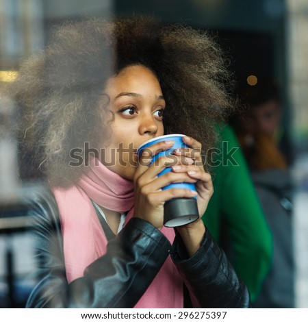 Young woman portrait drinking coffee inside a cafe. Image shot through a window.