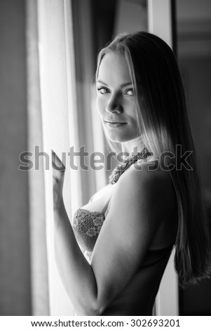 Sensual young woman portrait wearing lingerie at the window in hotel room. Black and white image.