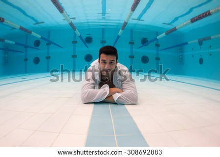 Man portrait with crossed arms wearing white shirt inside swimming pool. Underwater image.