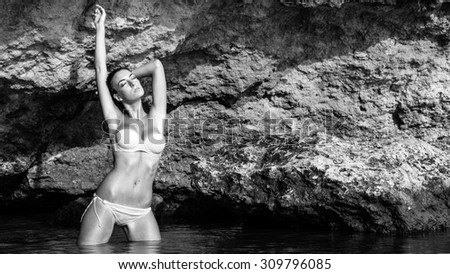Beautiful young woman portrait with rocks background on the beach. Black and white image.