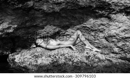 Beautiful young woman portrait laying on the rocks on the beach. Black and white image.