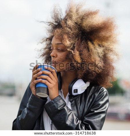 Young woman portrait outdoors on Westminster Bridge in London with coffee cup and headphones.