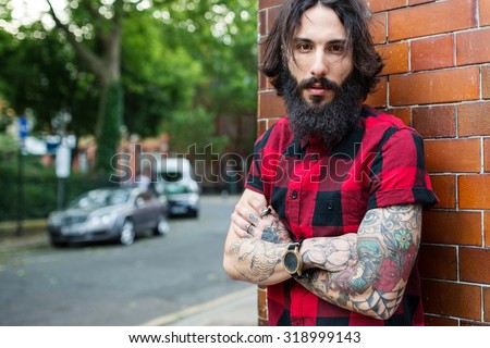 Close up portrait of young tattooed man standing with crossed arms in Shoreditch borough. London, UK. Hipster style.