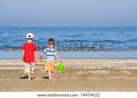 Two brothers walk along the beach in a sunny day.