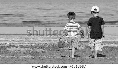 Two brothers walk along the beach in a sunny day. Black and white.