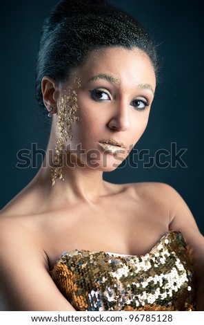 Beautiful woman with golden make up and dress against dark background.