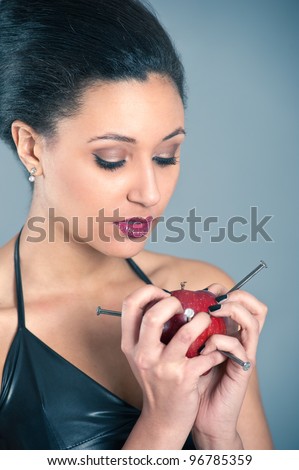 Conceptual image of beautiful girl with nails driven apple.