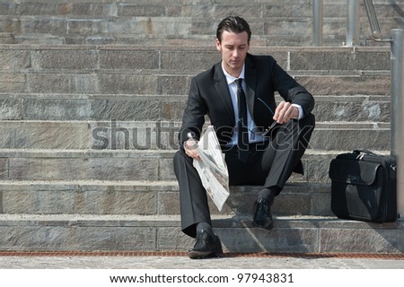 Young business man with newspaper sitting on the stairs.