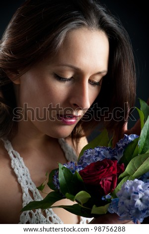 Portrait of beautiful woman smelling a flower\'s bouquet against black background.