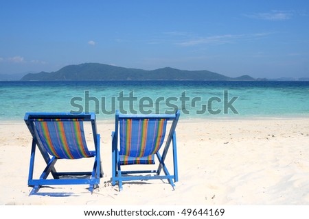 Two sunbeds staying lonely at the beach, view of the crystal clear water of Andaman Sea and the island. Made on Khai Nok Island, Thailand