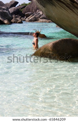 Young woman refreshing in water between rocks, water drops splash on head; crystal clear Andaman Sea, Similan Island, Thailand