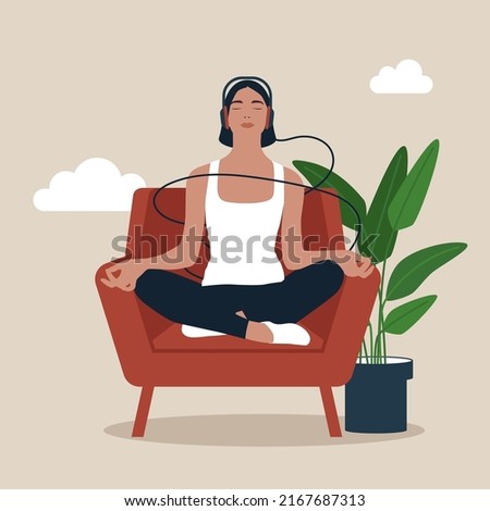 Full length mindful young woman making mudra gesture, sitting in lotus position on comfortable couch at home. Peaceful millennial girl deeply meditating, doing breathing yoga exercises alone.