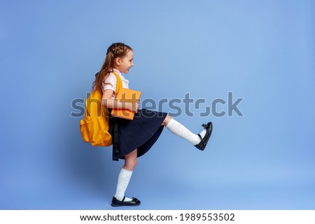 Cute happy kid in uniform. raises his leg high and runs on purple background. child with backpack. little girl is ready for school. Dynamic images that go back to conceptual school. holidays begin.