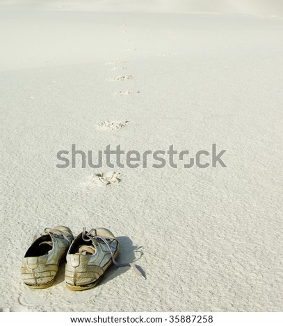 Abandoned shoes on white sand leaving footprints going infinitely