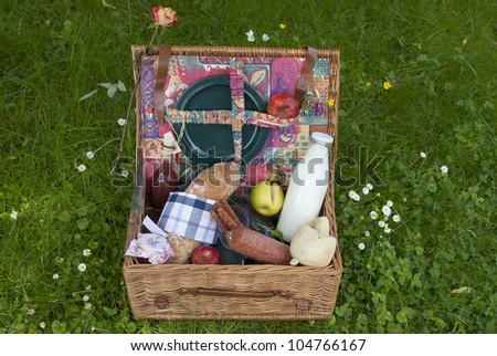 picnic basket on lawn  with fresh olive-baguette, milk, apple and sausages, bread and  pieplant juice.
