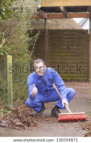 man at work.   groundskeeper (caretaker service) cleaning a garden path.  positive expression with thumb up.