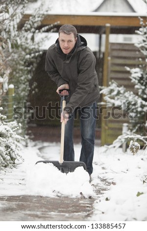 after a snowstorm. man with a black shovel to removes the snow from a house entrance.