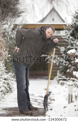 man at work. groundskeeper (caretaker service) removing snow with a shovel. having backache after hard work.