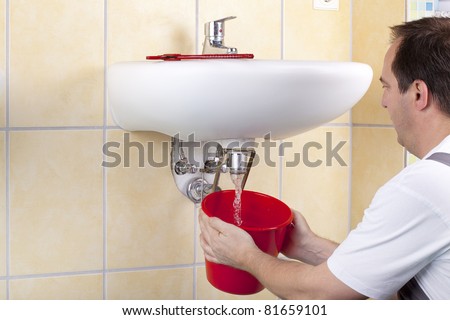 studio-shot of a plumber repairing the drain of a sink and changing a clogged pipe. the plumber is flushing the drain.