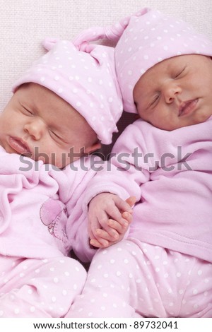 studio-shot of identical ( similar ) newborn babies. twin sisters sleeping and holding hand.