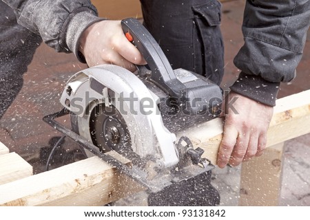 studio-shot of a carpenter cutting wood with electric saw,  for furniture.