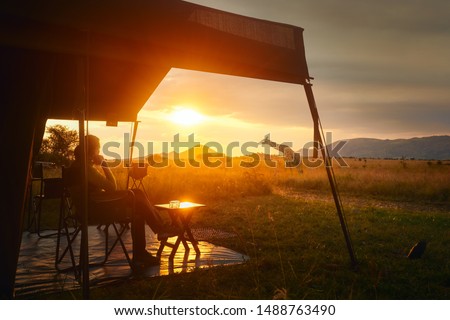 Woman rests after safari in luxury tent during sunset camping in the African savannah of Serengeti National Park, Tanzania.Woman Camping Tent Savanna Outdoors Concept